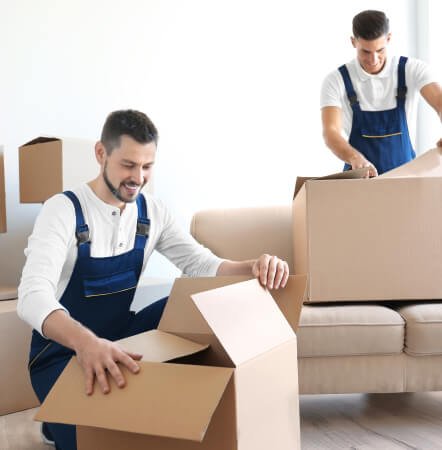 Two logistics warehouse workers wearing blue uniforms carefully packing items into cardboard shipping boxes.